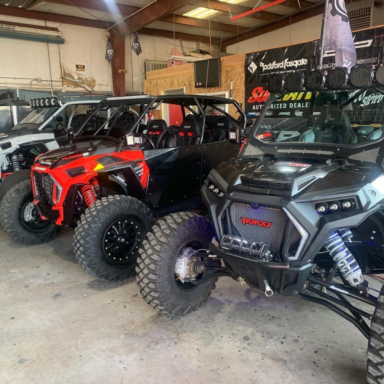 Red and black all-terrain vehicles displayed in a garage shop with equipment and signage visible in the background