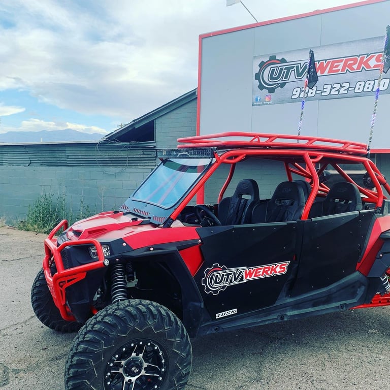 Red and black UTV with open doors and roof rack parked in front of UTV Werks garage building