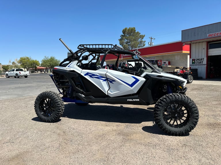 Black and white Polaris RZR off-road vehicle with large tires parked in a lot with a red building visible