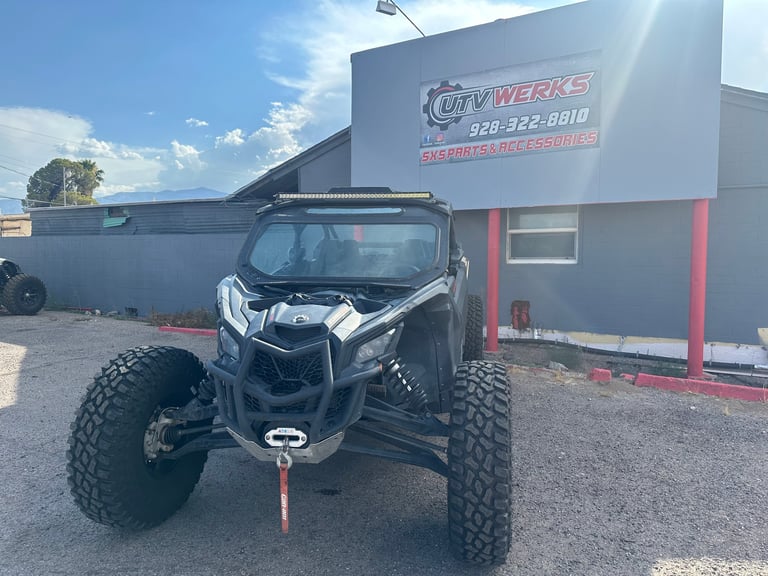 Modified black UTV with large tires and roll cage parked in front of City Werks shop building