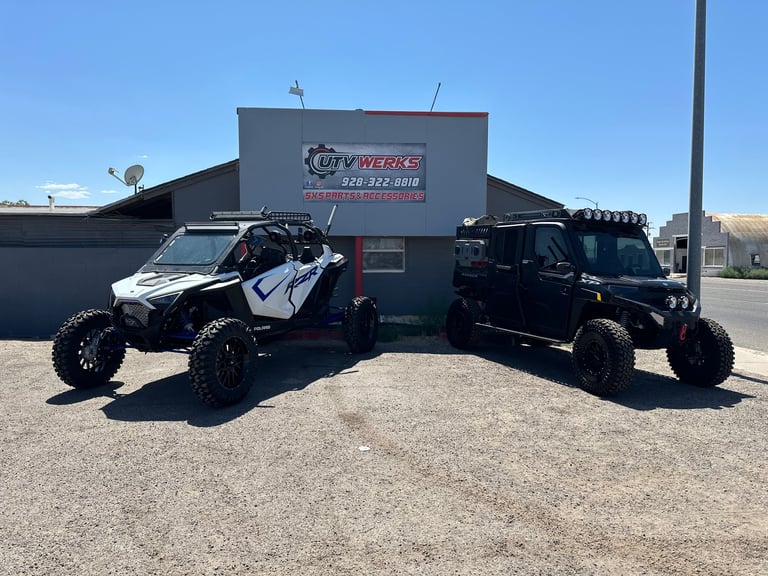Two black and white all-terrain vehicles parked in front of an off-road shop building with clear sky background