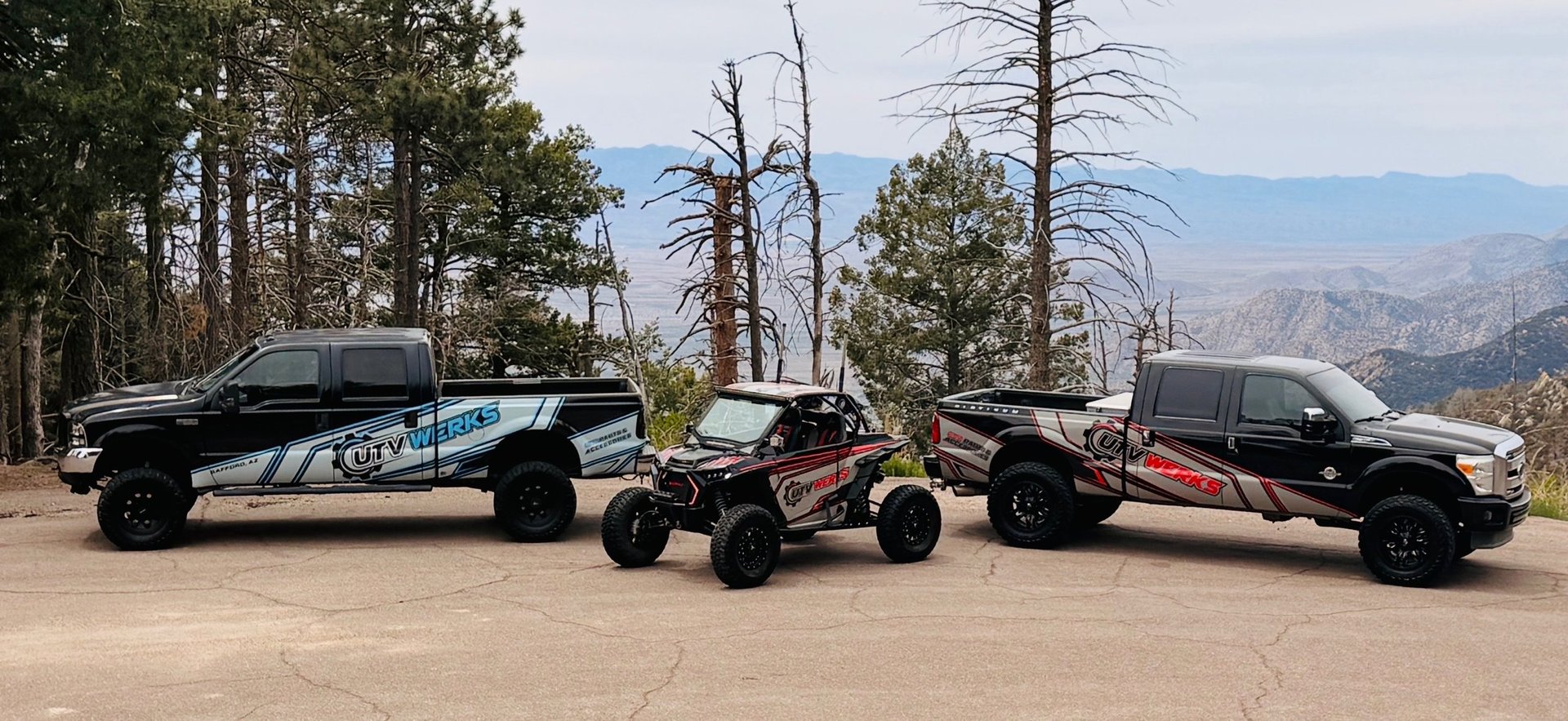 Three custom-built off-road vehicles lined up in a desert mountain landscape with dead trees
