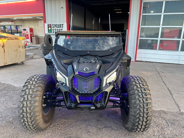 Blue and purple UTV with large knobby tires parked in front of a commercial storefront