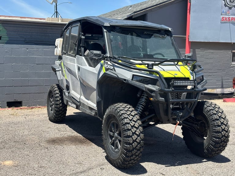 Modified white and yellow utility vehicle with lifted suspension and large off-road tires parked outdoors
