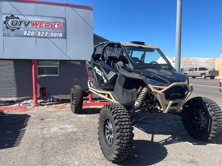 Black and tan custom off-road buggy with large tires parked outside City Werks shop with red trailer