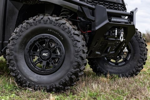 Close-up of black off-road vehicle wheels with large knobby tires and custom rims parked on grass