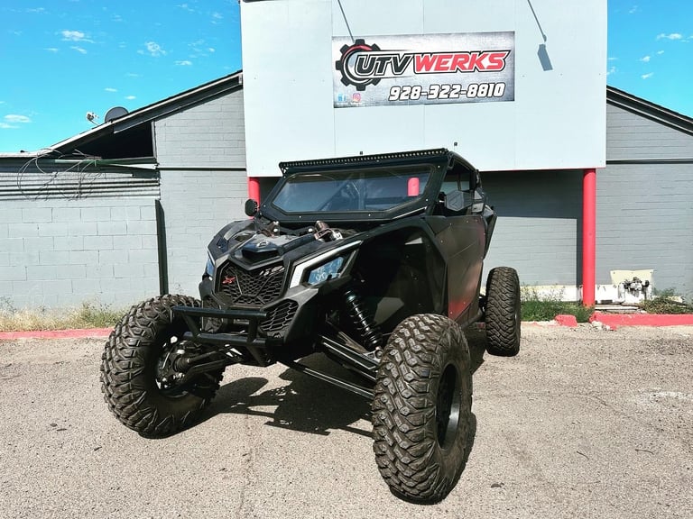 Black all-terrain vehicle with large knobby tires parked in front of ATV Werks shop building