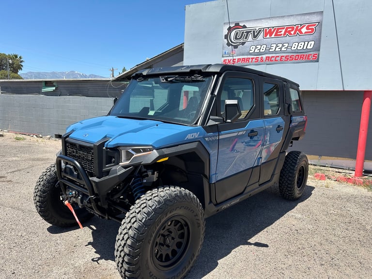 Blue and black lifted UTV side-by-side vehicle with rugged tires displayed at an off-road equipment dealer lot