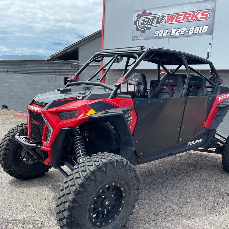 Red and black side-by-side ATV with roll cage parked outside UTV Werks shop building