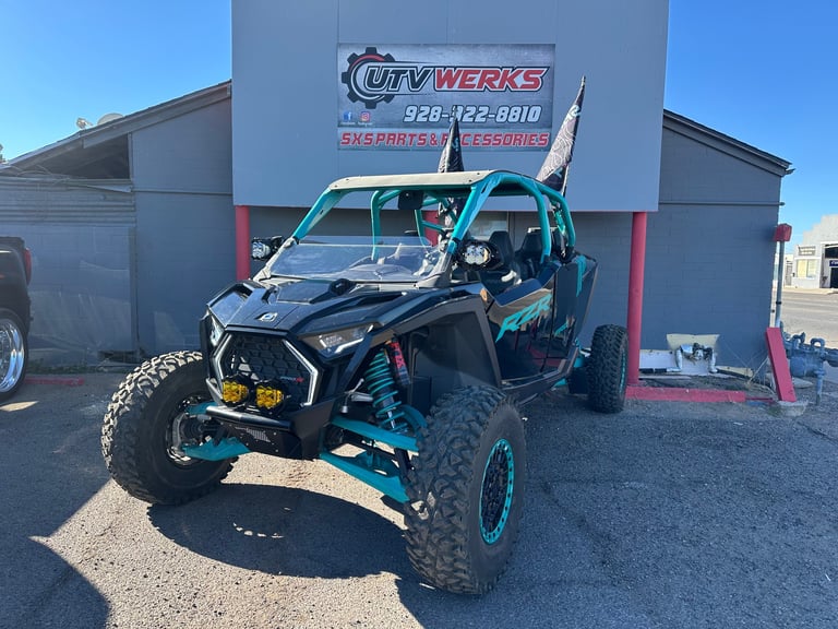 Custom black and turquoise UTV with open frame design parked in front of UTV Werks shop with metal building